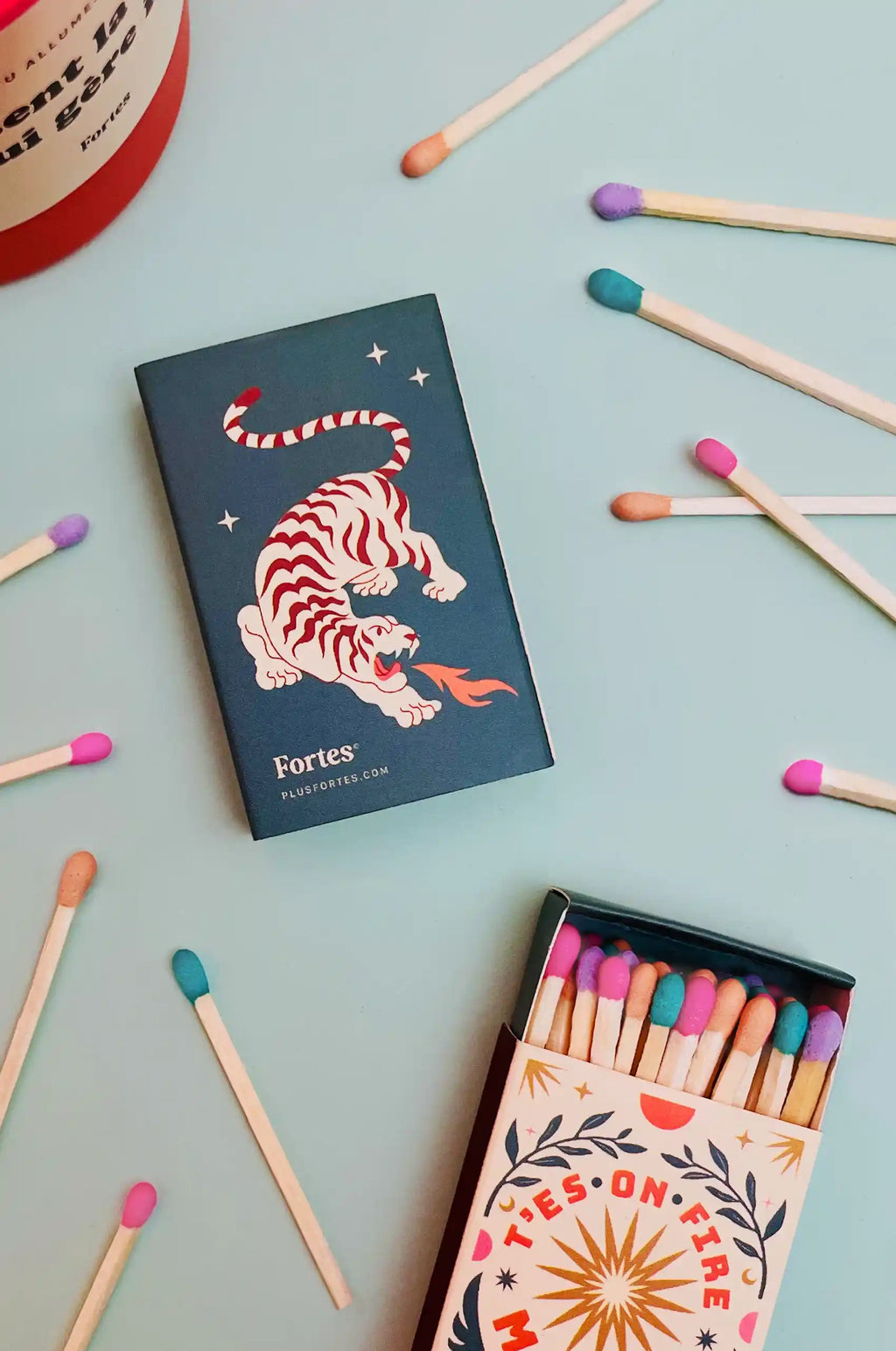 Petites boîtes d’allumettes Fortes avec motif de tigre, dont une ouverte, parmi des allumettes multicolores