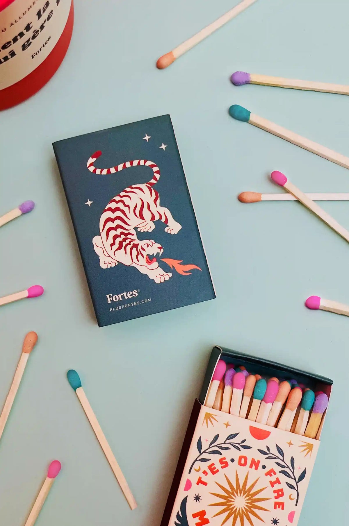 Petites boîtes d’allumettes Fortes avec motif de tigre, dont une ouverte, parmi des allumettes multicolores