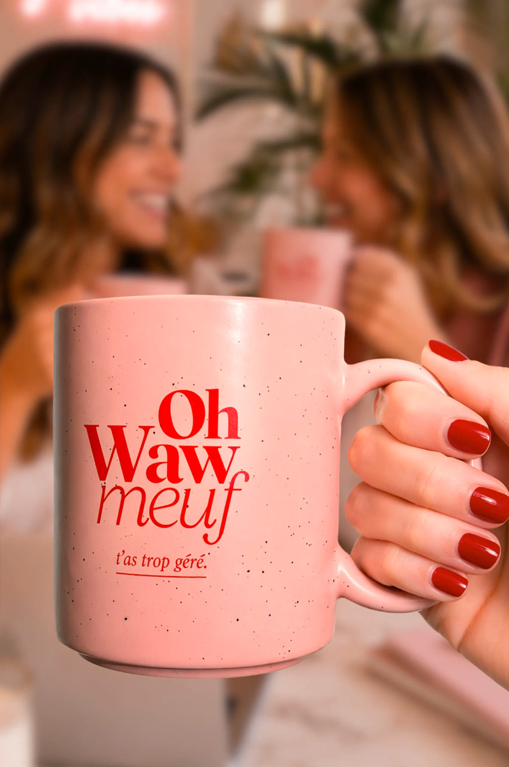 Tasse rose Fortes « Oh Waw meuf » tenue au premier plan, devant deux femmes buvant dans des tasses