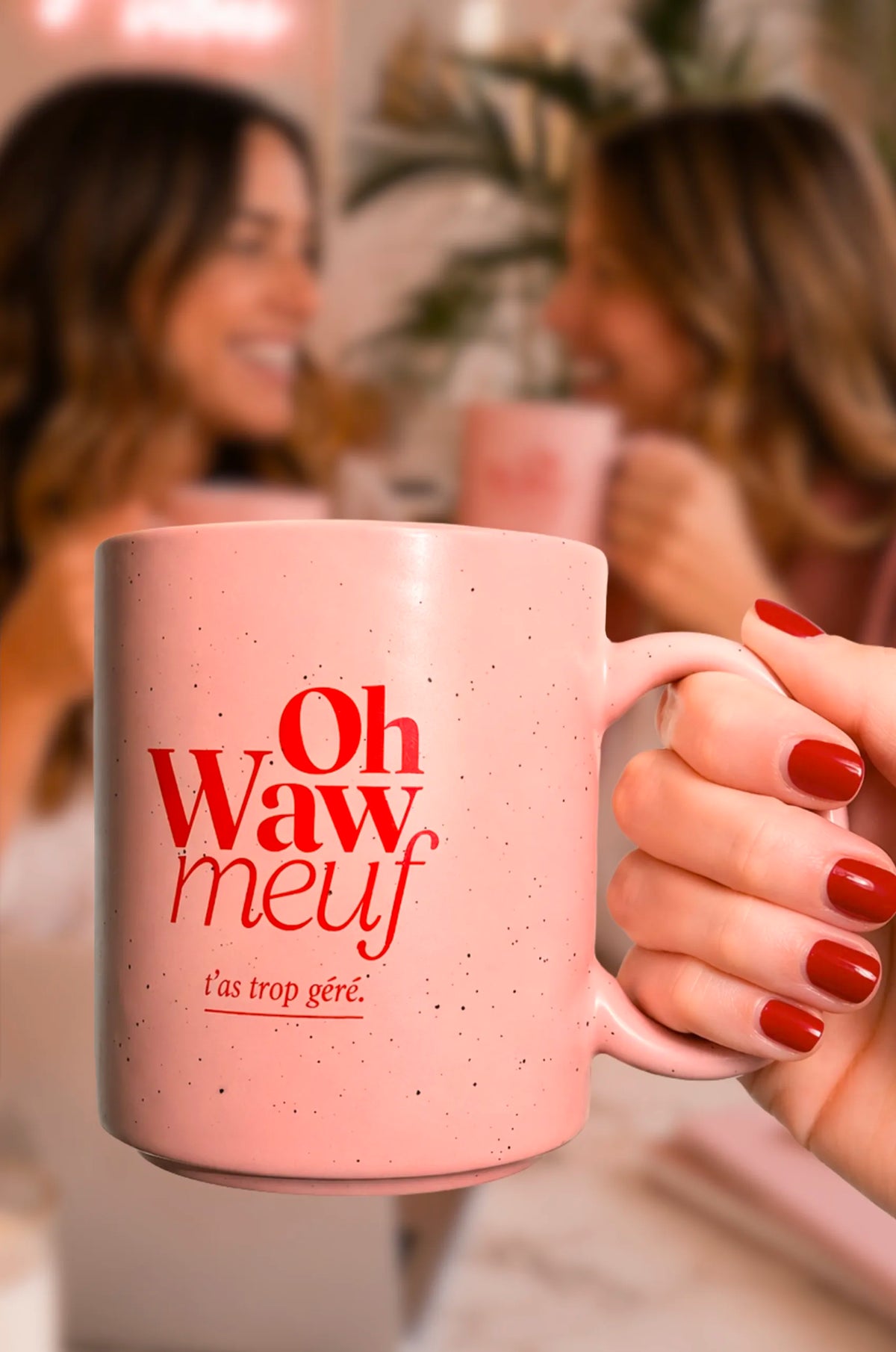 Tasse rose Fortes « Oh Waw meuf » tenue au premier plan, devant deux femmes buvant dans des tasses