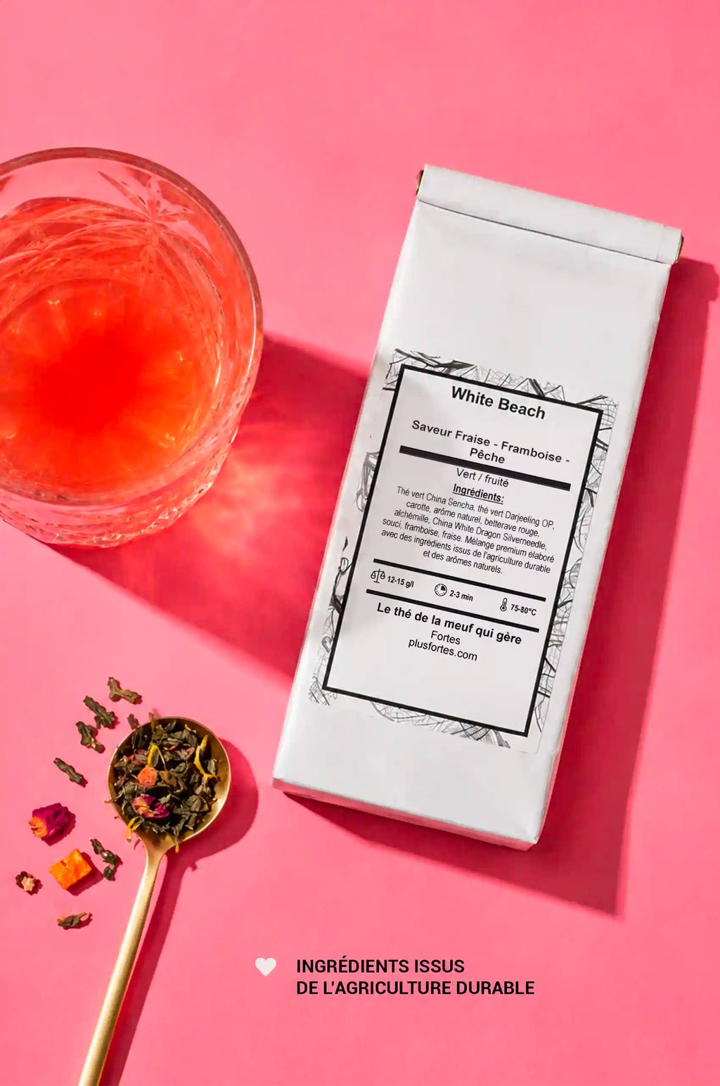 Vue de dessus du sachet de thé Fortes, d’un verre de thé et d’une cuillère de mélange, sur fond rose
